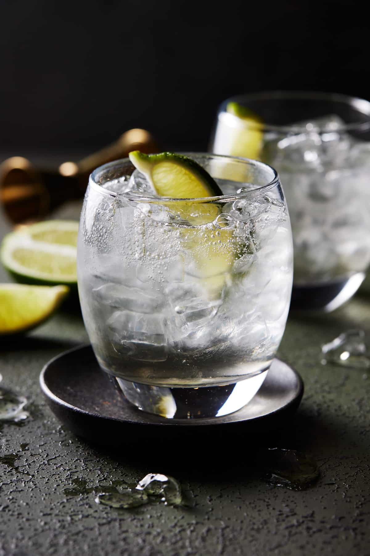 Elderflower Gin & Tonic cocktail in lowball glass on a dark coaster with lime wedge. 