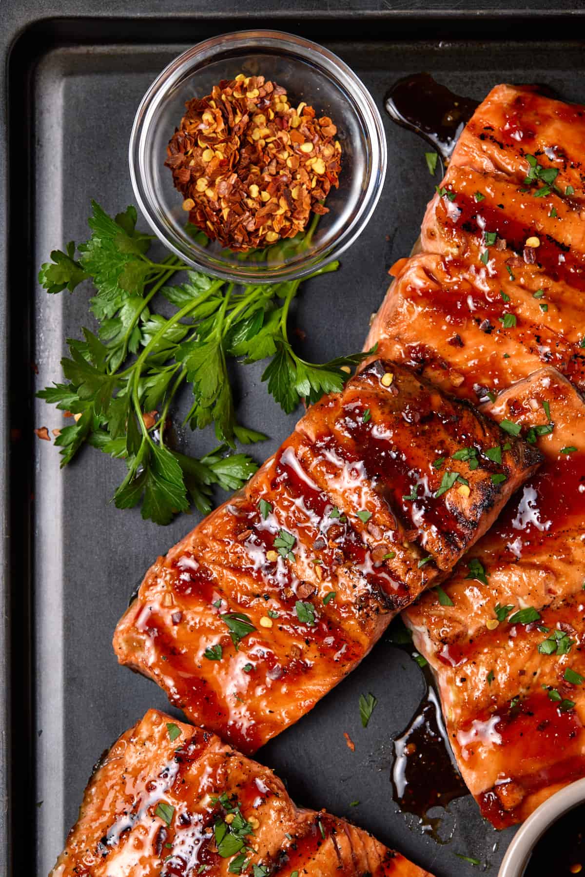 Grilled sockeye salmon fillets on black sheet pan with crushed red pepper & parsley. 