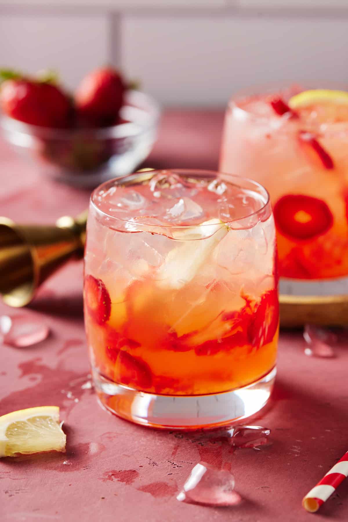 Two lowball glasses filled with strawberry vodka lemonade on a pink board.