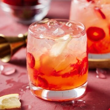 Lowball glass of Strawberry Vodka Lemonade on a pink board.