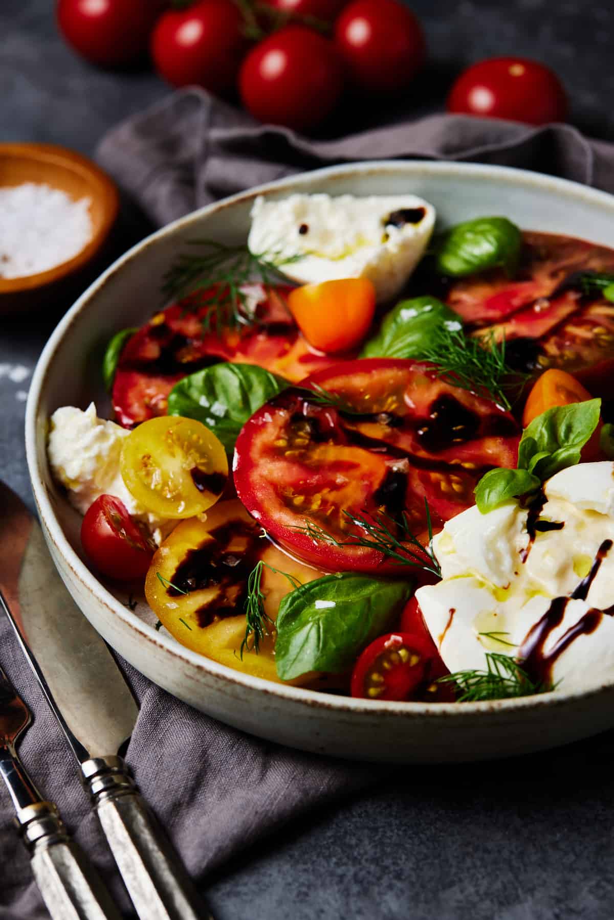 Bowl of burrata caprese salad garnished with fresh herbs. 