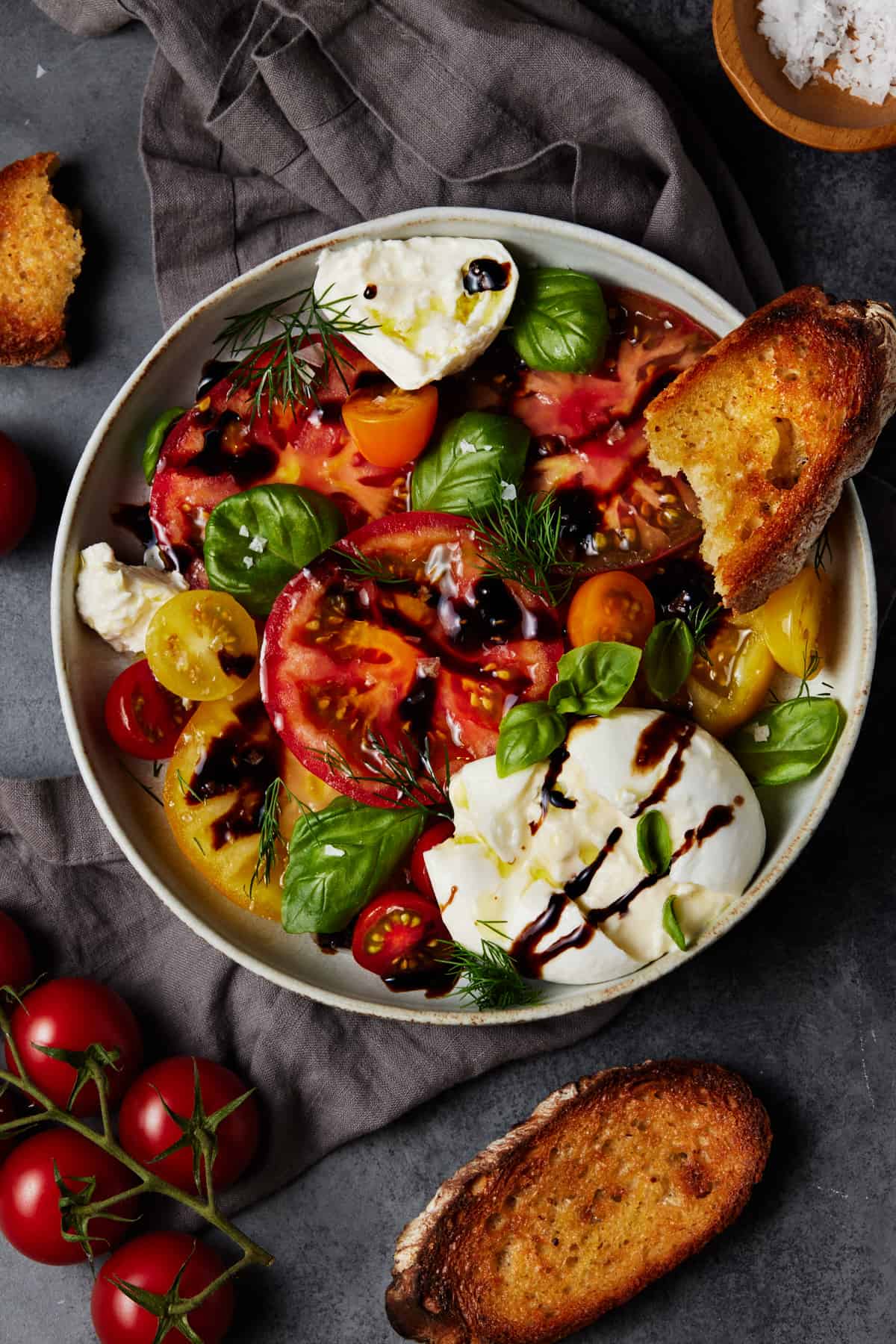 Burrata caprese salad in light gray bowl with crostini. 