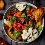 Large bowl filled with burrata caprese salad with crostini.