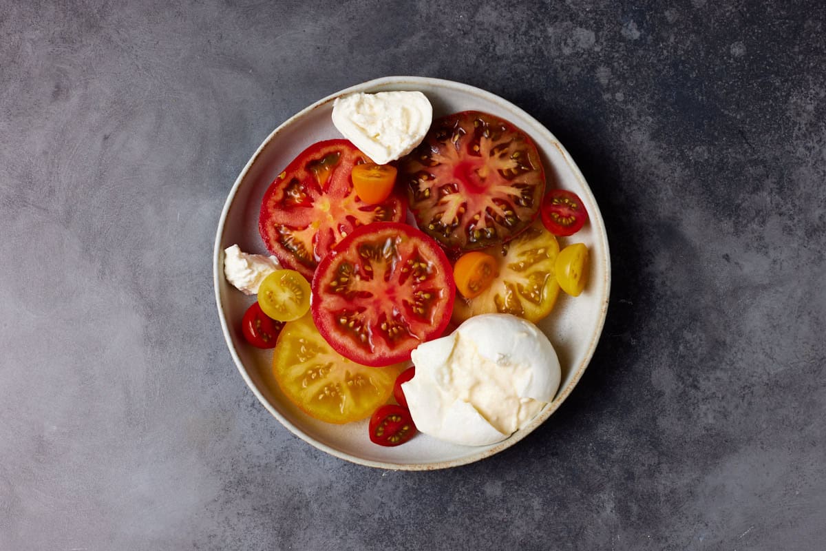 Sliced heirloom tomatoes and burrata cheese in a shallow bowl. 