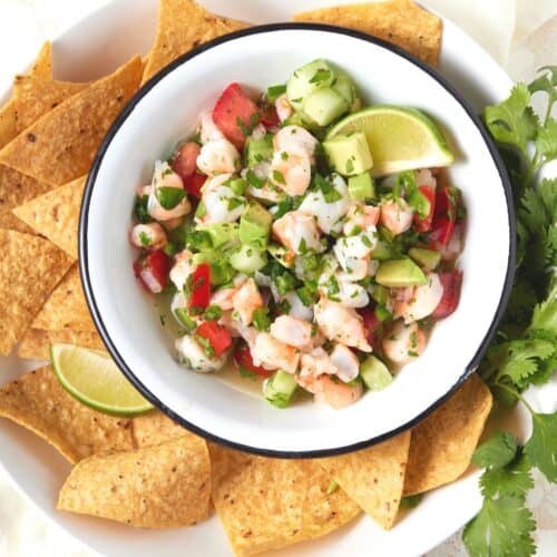 Bowl of ceviche de camaron with tortilla chips and lime wedges.