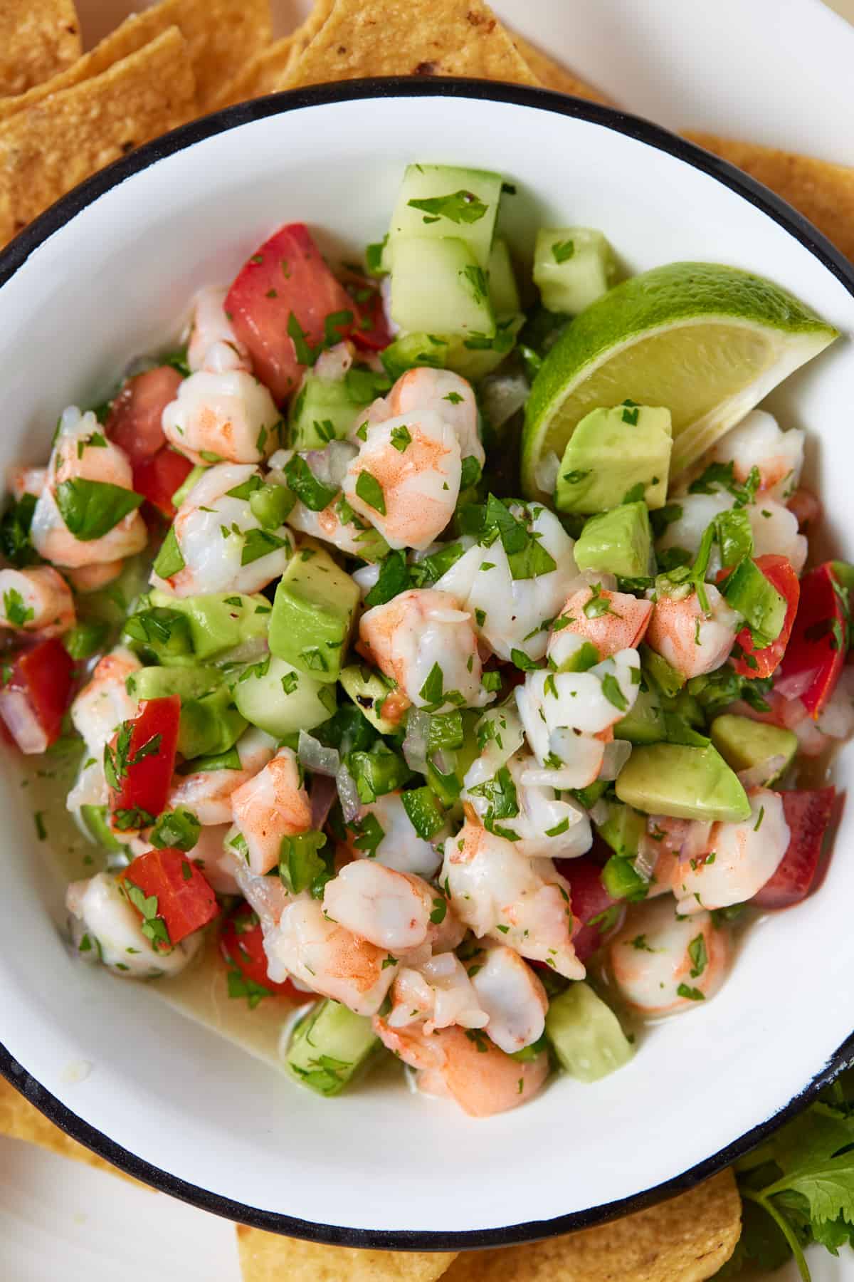 Shrimp ceviche in bowl with fresh veggies and lime wedge.