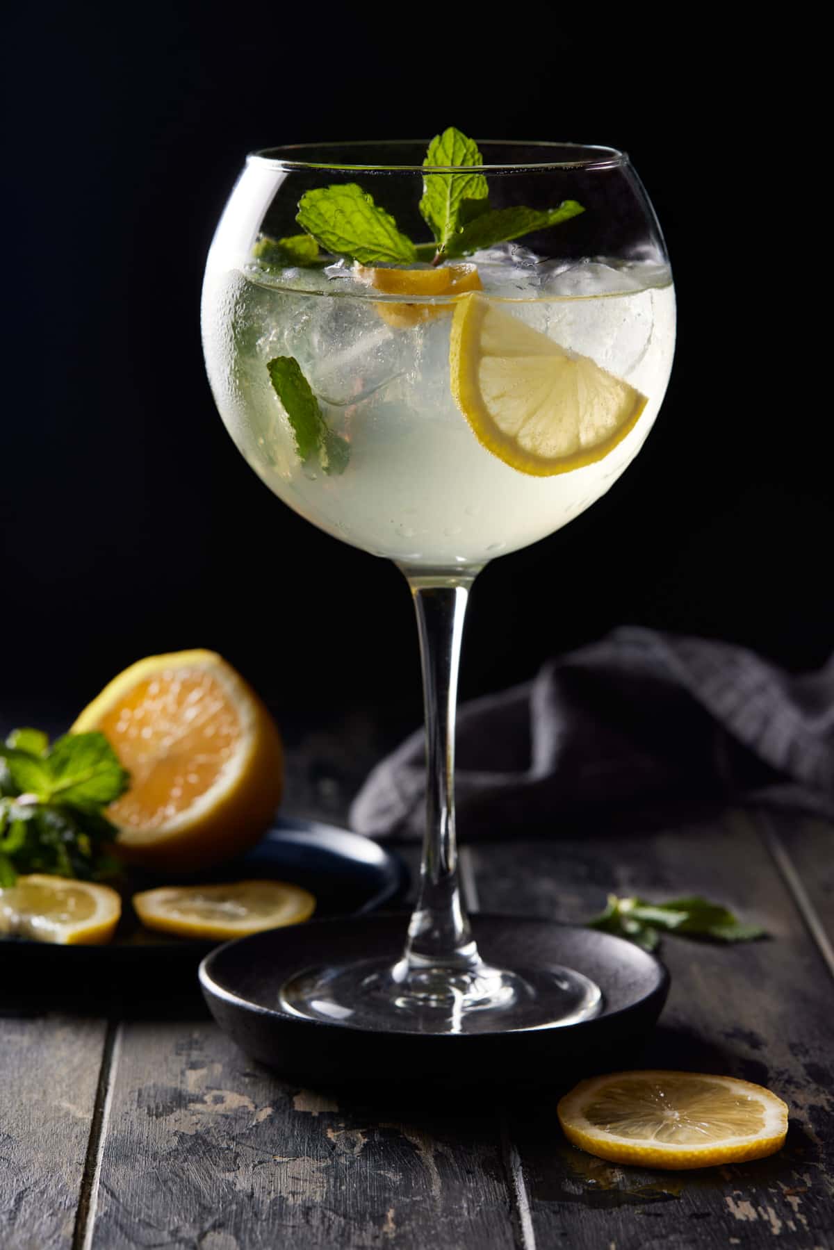 Tall wine glass filled with ice, lemon, mint and bubbly hugo spritz drink. 