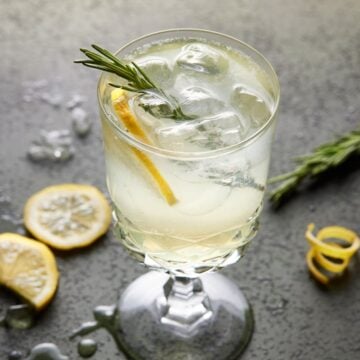 Footed glass filled with limoncello spritz cocktail, lemon slices and fresh rosemary.