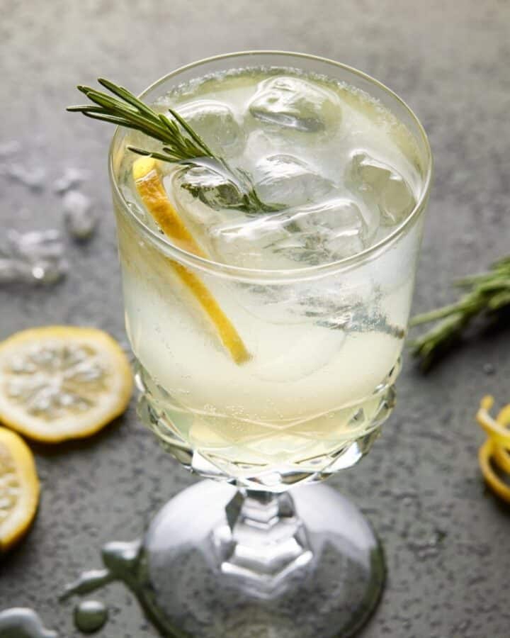 Footed glass filled with limoncello spritz cocktail, lemon slices and fresh rosemary.