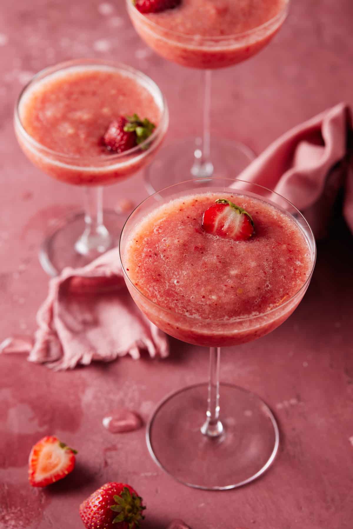 trio of frozen rosé filled glasses on pink board with fresh strawberries.