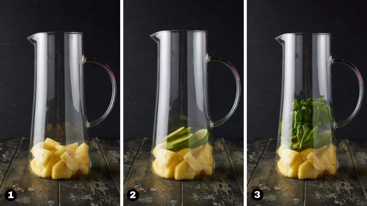 A glass pitcher filled with pineapple, lime slices and basil leaves. 