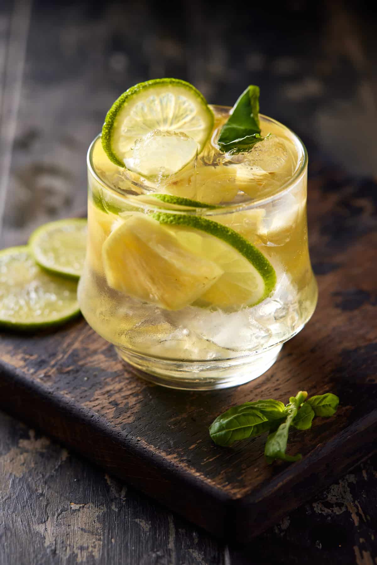 Lowball glass filled with white wine sangria, pineapple and lime slices on a wood board. 