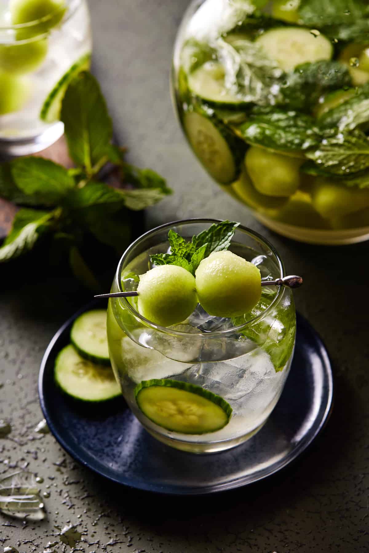 Spa Water Sangria in both a glass and pitcher garnished with honeydew melon and cucumber slices. 