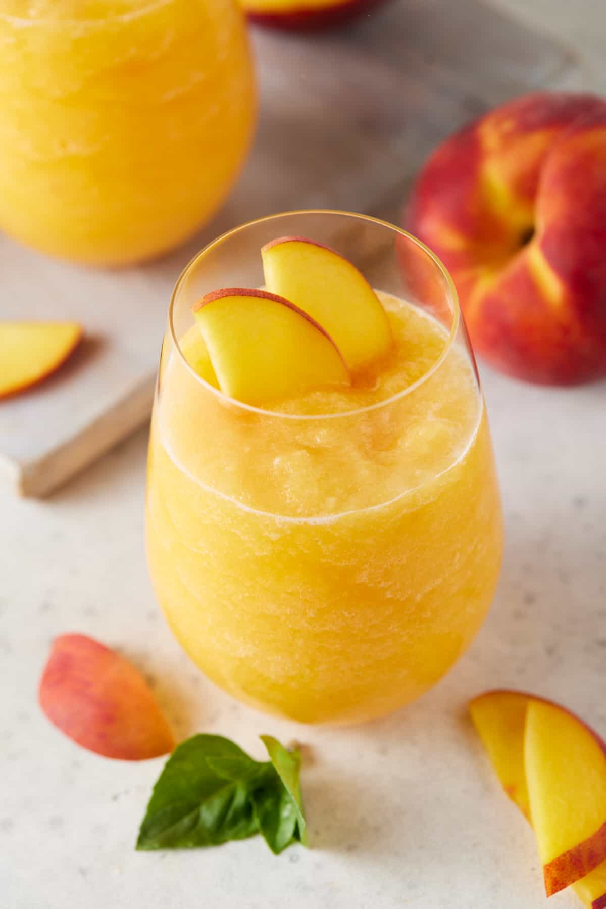 Peach wine slushie in a stemless wine glass garnished with fresh peach slices.