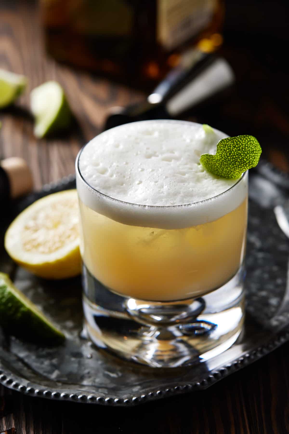 Tequila sour with lime peel and jigger on tray.