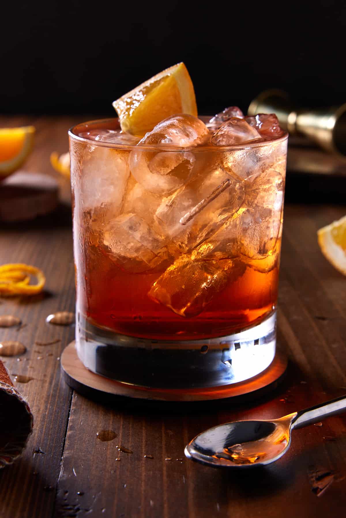 Lowball glass filled with bourbon and aperol cocktail and garnished with orange wedge. 