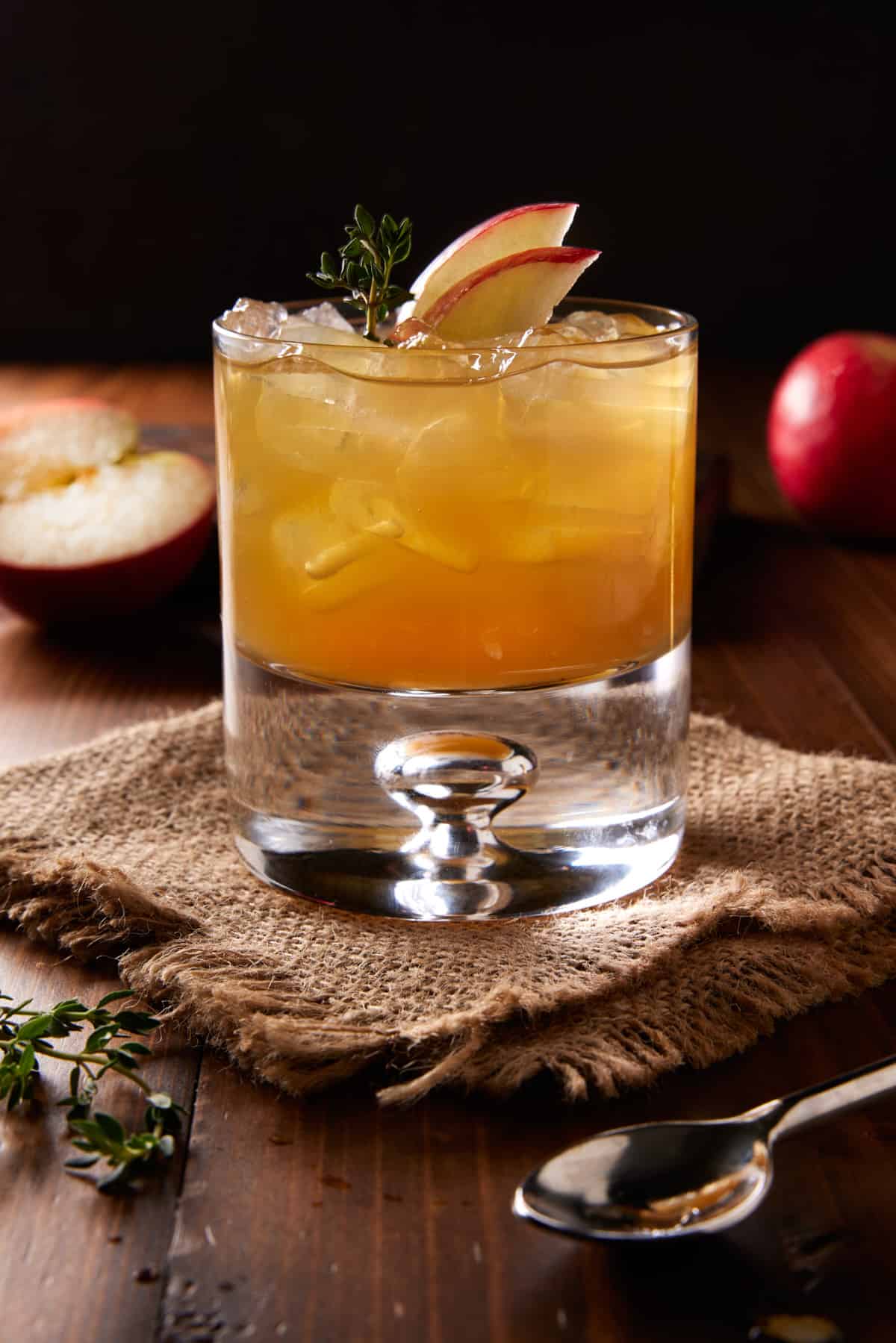 Lowball glass of apple cider bourbon cocktail with fresh apple slices and thyme sprigs. 