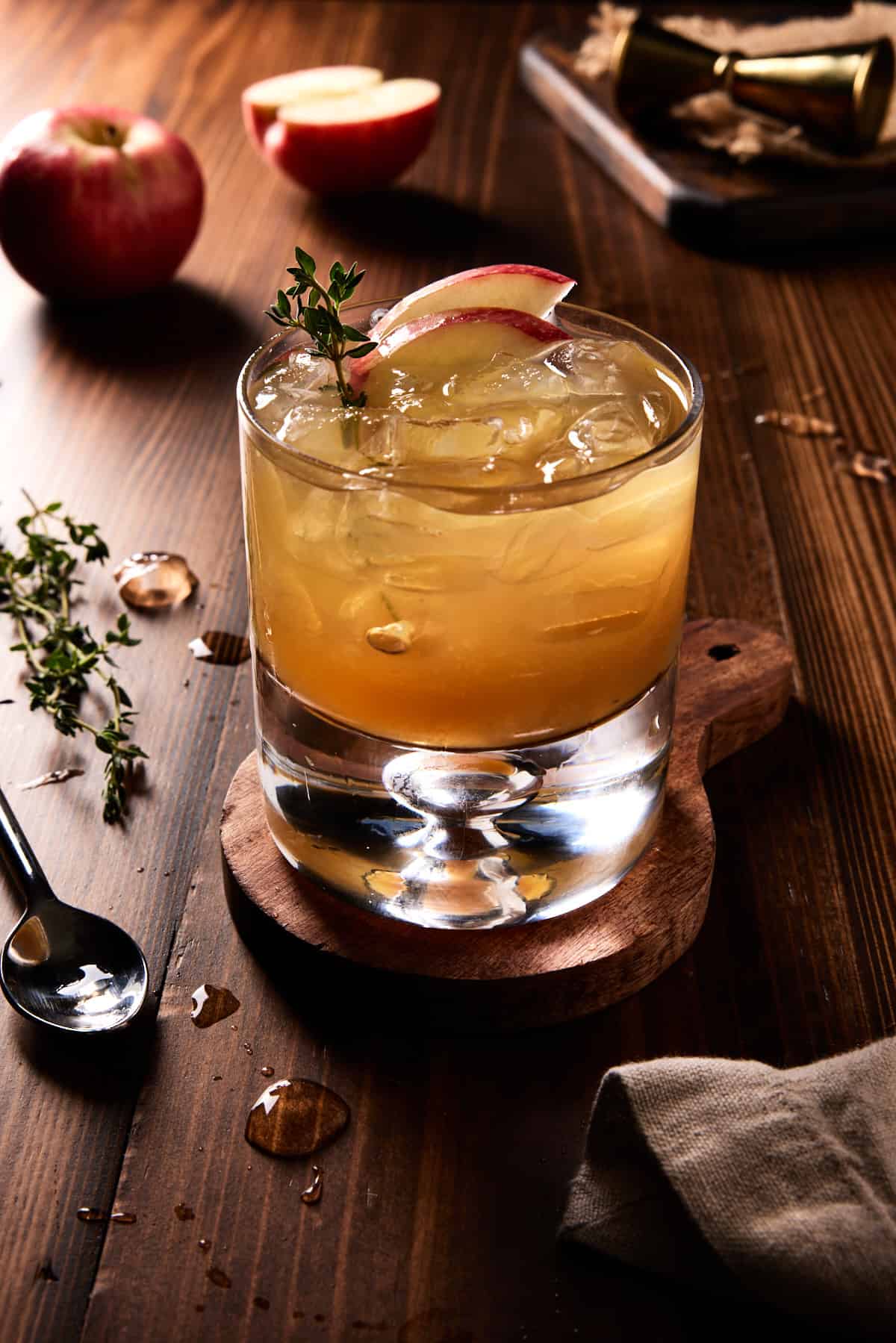 Lowball glass of apple cider bourbon cocktail garnished with fresh thyme and apple slices. 