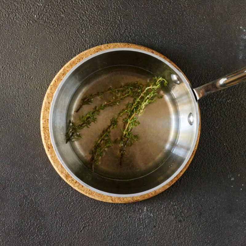 A saucepan filled with simple syrup and fresh thyme. 