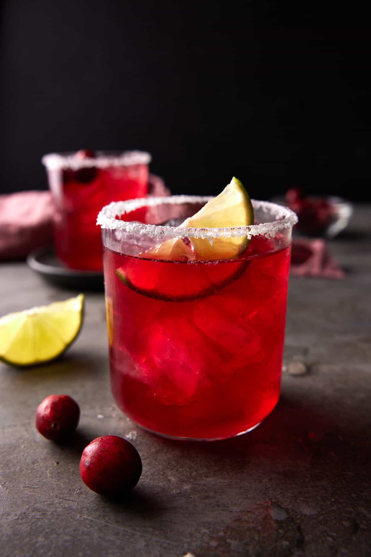Cranberry Margaritas in low ball glasses rimmed with salt and a lime wedge.
