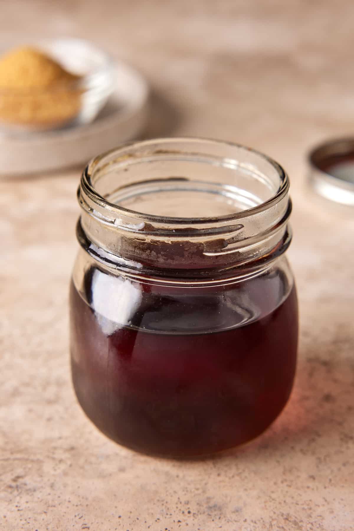 Cocktail syrup in a jar with sugar in the background.