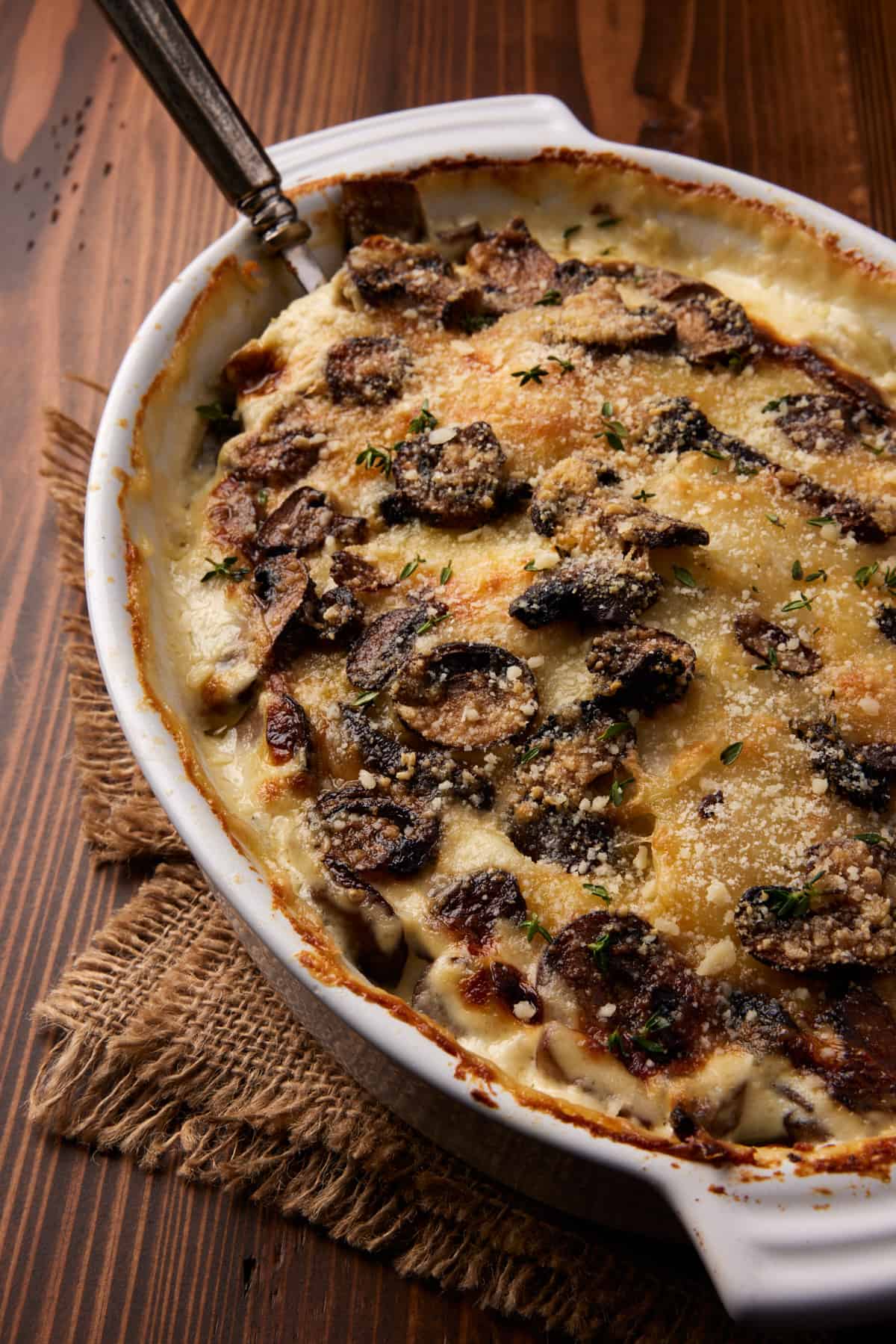 Potato and Mushroom gratin sprinkled with parmesan cheese in a white baking dish.
