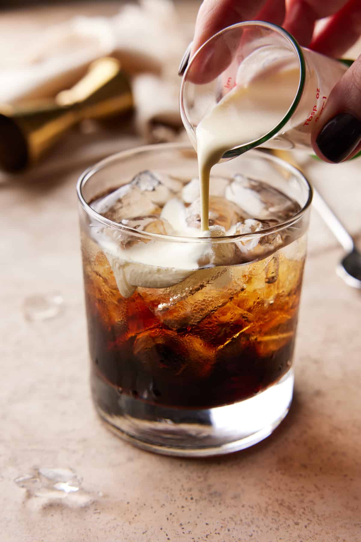 Low ball cocktail glass filled with ice and kahlua with cream being poured in.