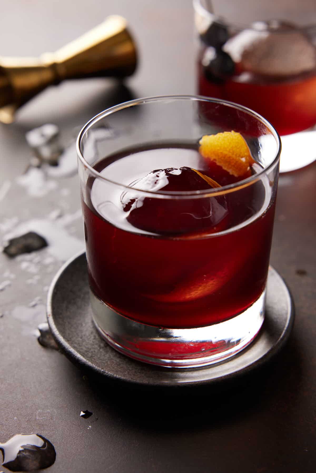 Brandy Old Fashioned with orange peel in a low ball glass with jigger in background.