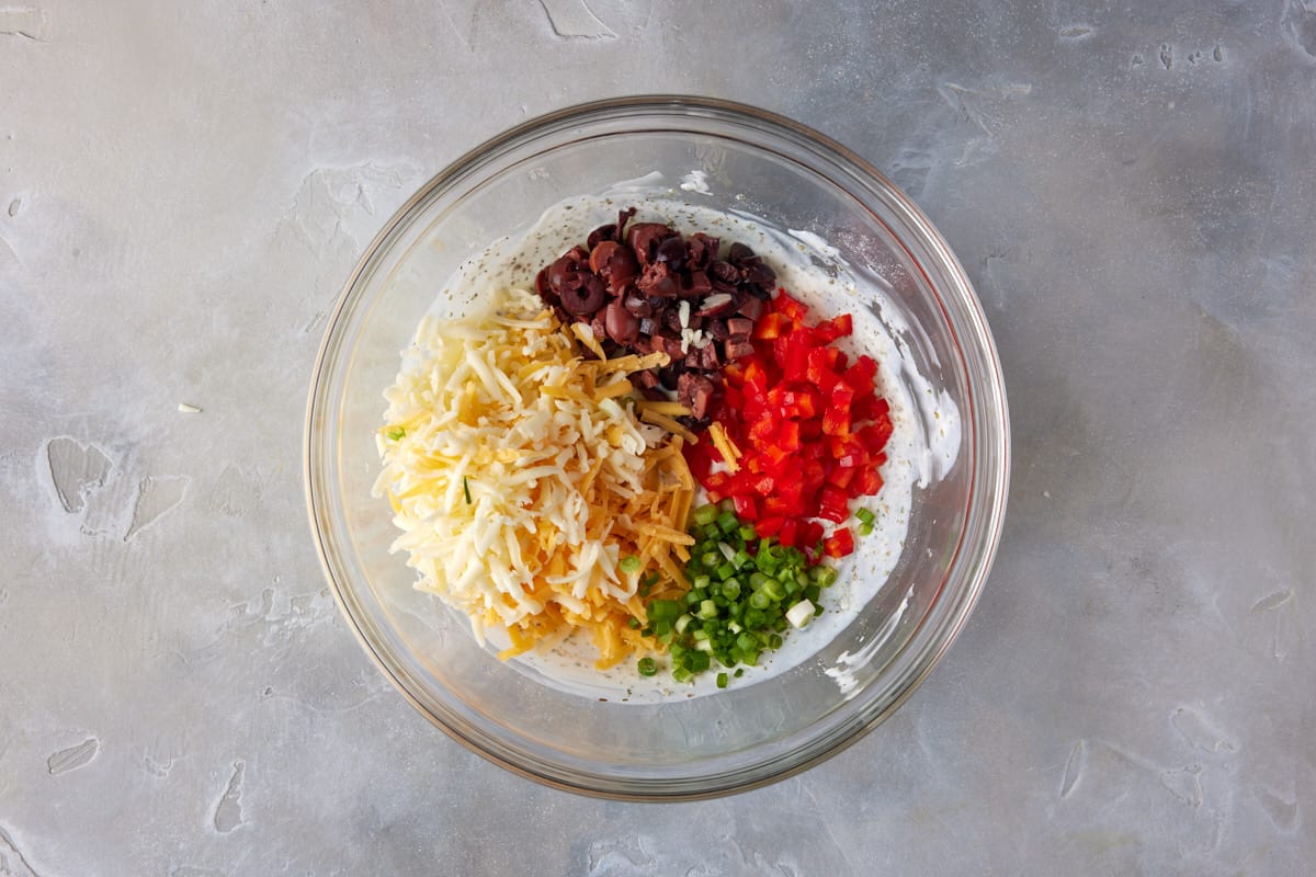 Cheeses and chopped vegetables in bowl with buttermilk mixture.