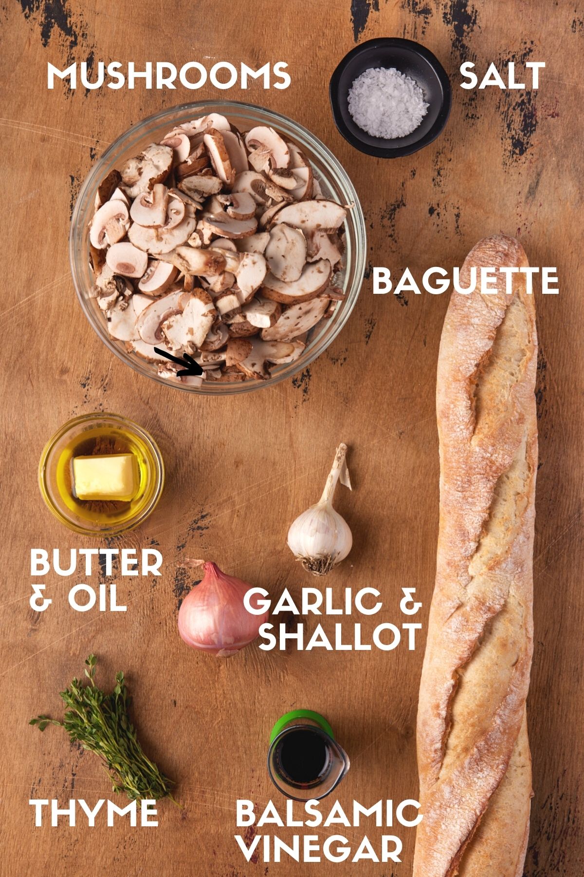 Ingredients for mushroom bruschetta on wood board, including a baguette, mushrooms and thyme. 