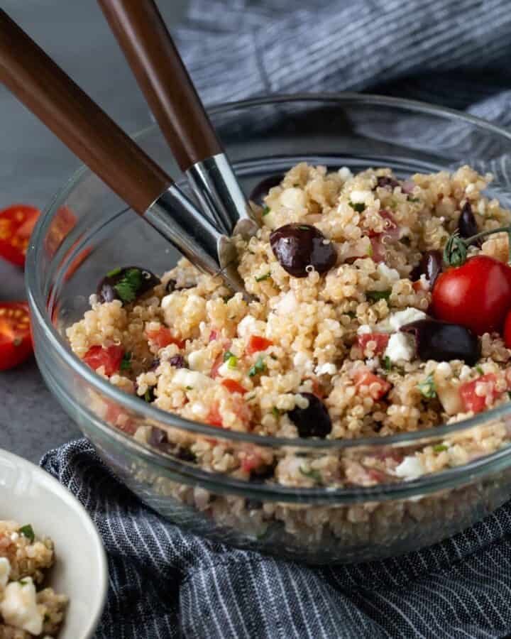 Glass bowl filled with quinoa salad and two spoons.
