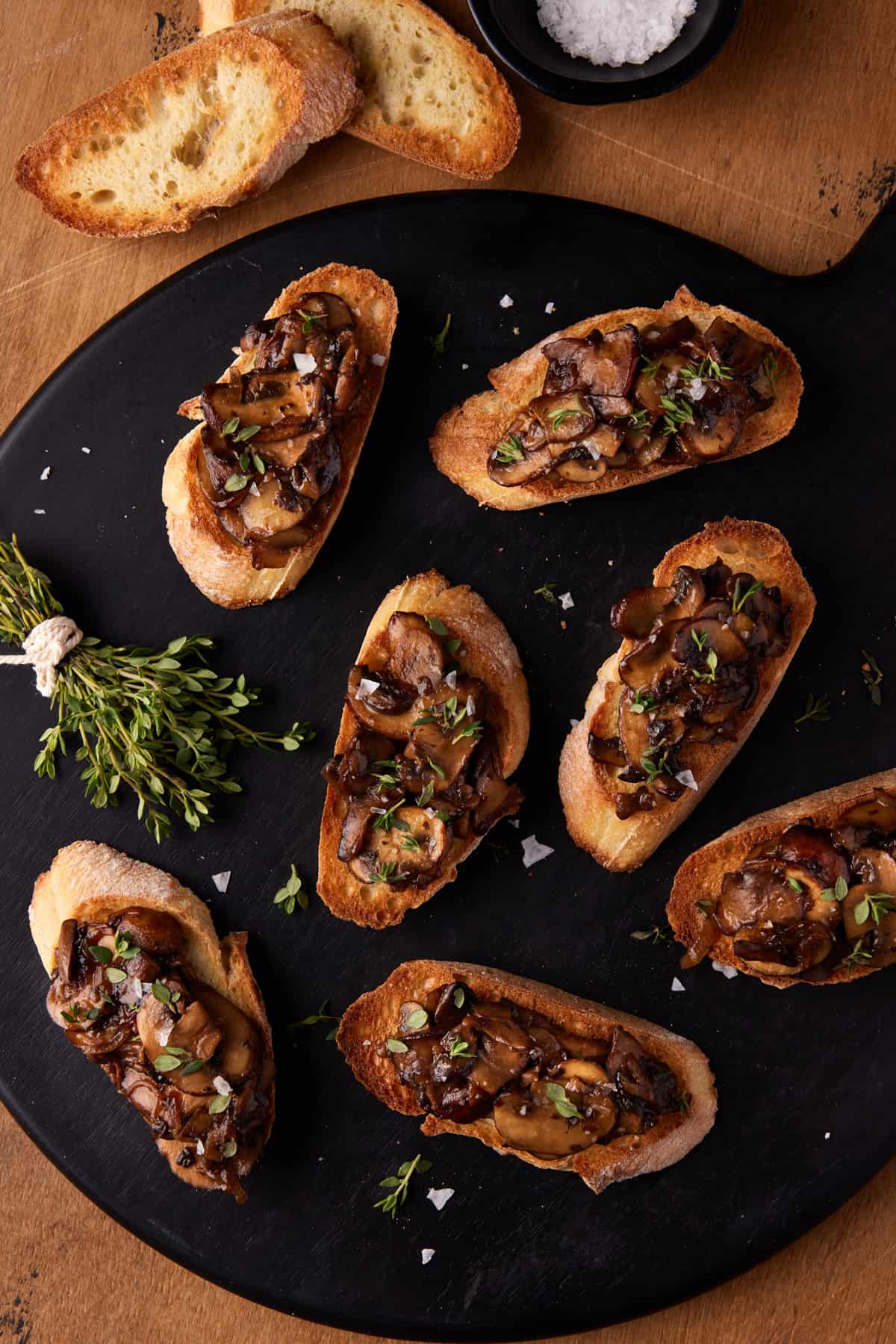 Black round board with slices of mushroom bruschetta and fresh thyme. 