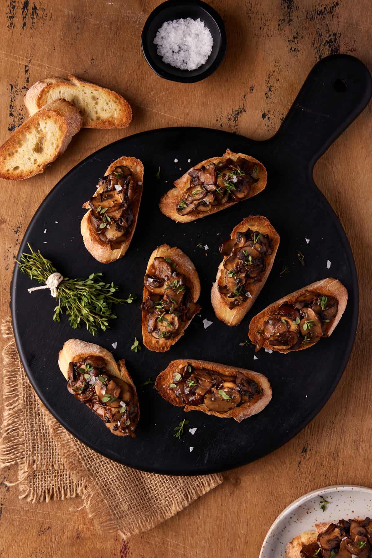 Black round cutting board filled with mushroom bruschetta. 