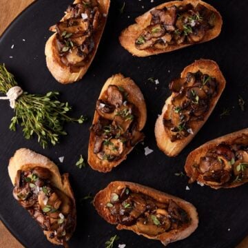 Black cutting board filled with mushroom bruschetta.