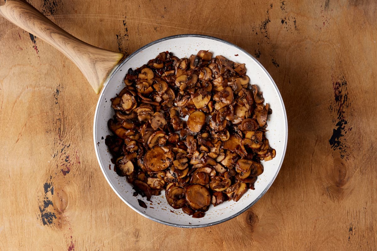 White skillet with sliced mushrooms sauteed with balsamic vinegar.