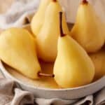 Poached pears in a cream and tan flecked bowl.