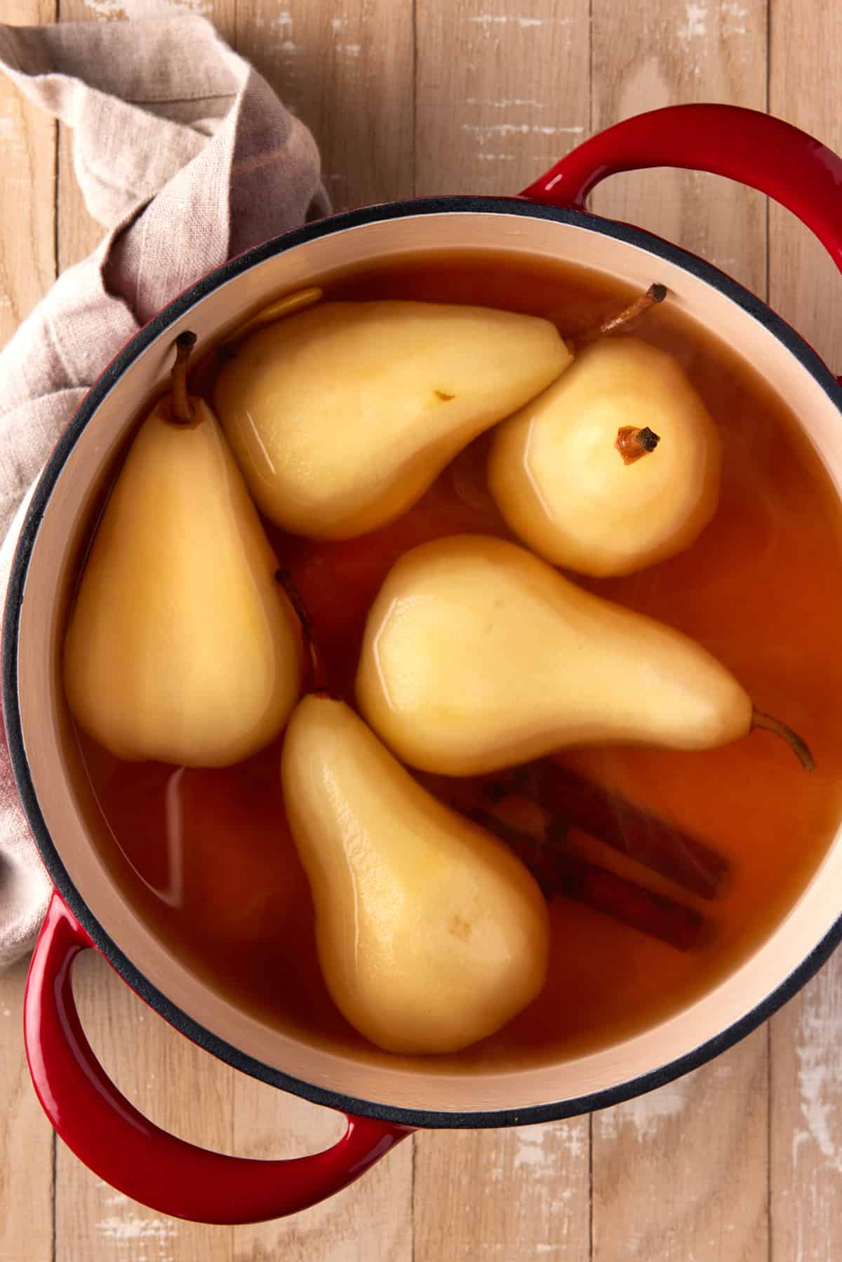 Poached pears in poaching liquid in a red dutch oven. 