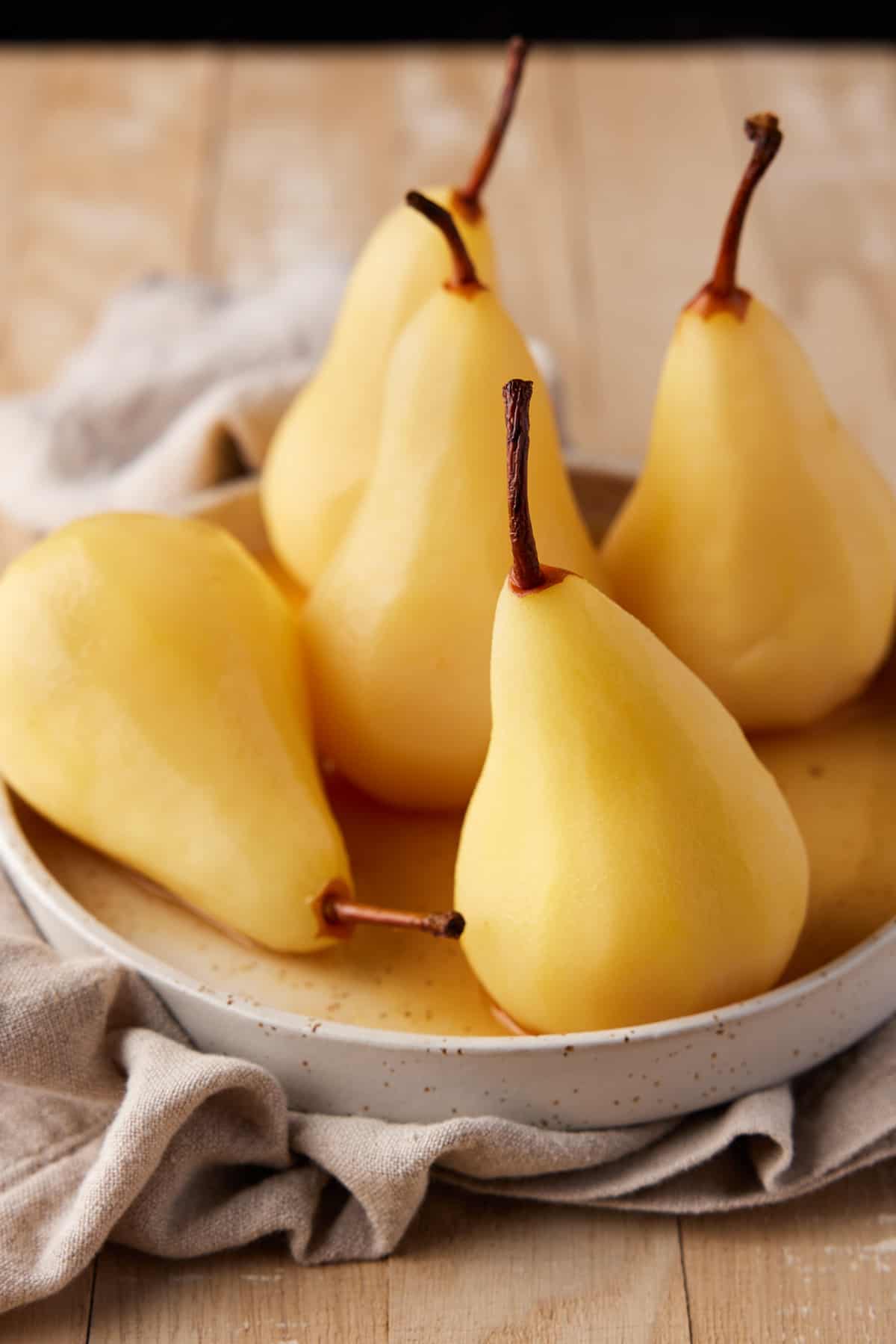Poached pears on a tan plate with an oatmeal colored napkin. 