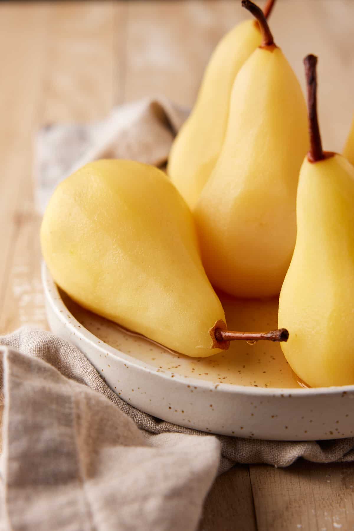 Close up of poached pears on a tan plate. 