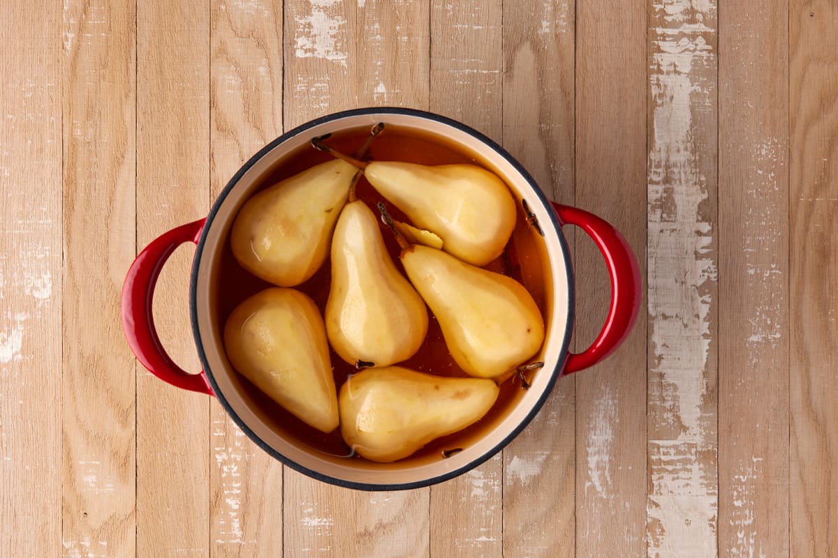 Peeled pears in poaching liquid in red dutch oven. 