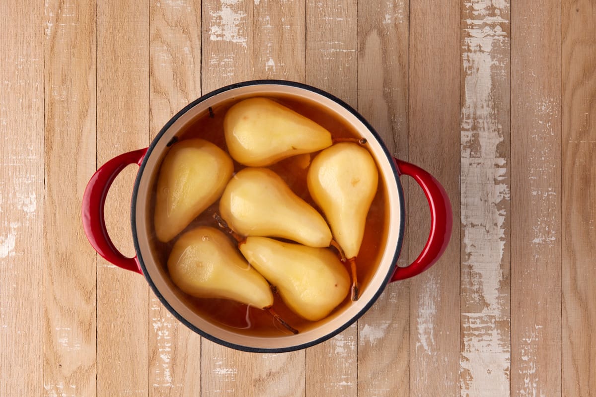 Poached pears in poaching liquid in red dtuch oven. 