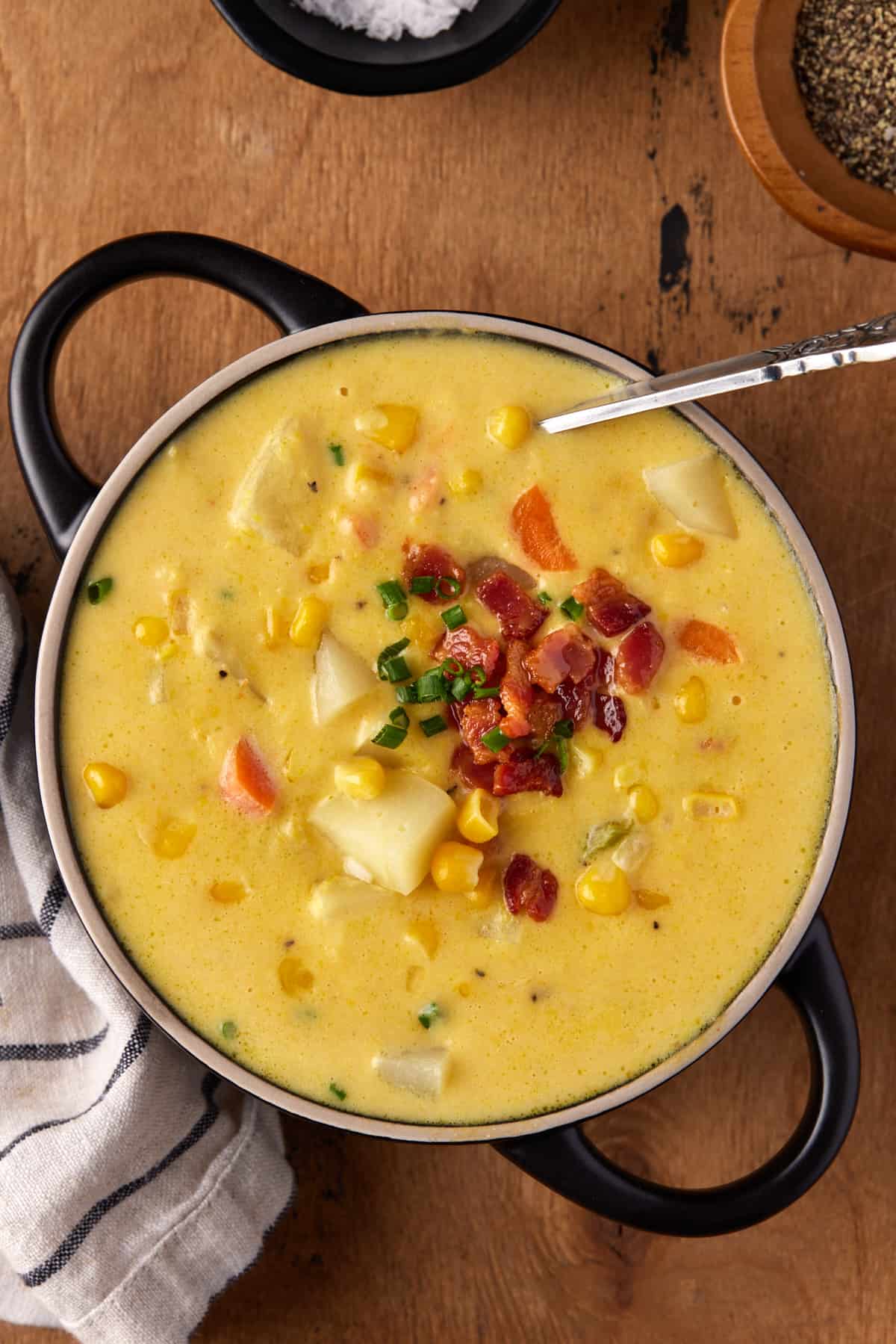 Black soup bowl filled with potato corn chowder with a spoon in it. 