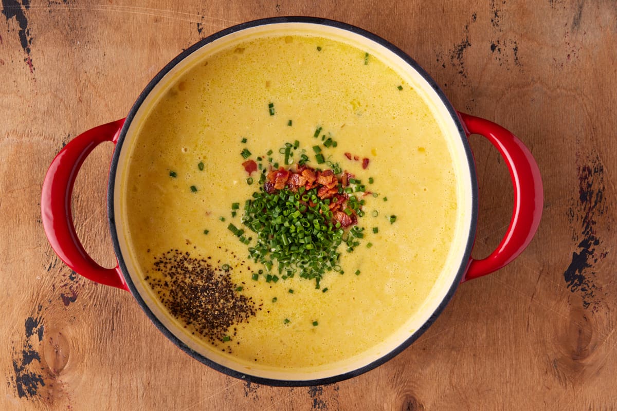 Red dutch oven with potato corn chowder and garnished with chives, bacon and black pepper. 