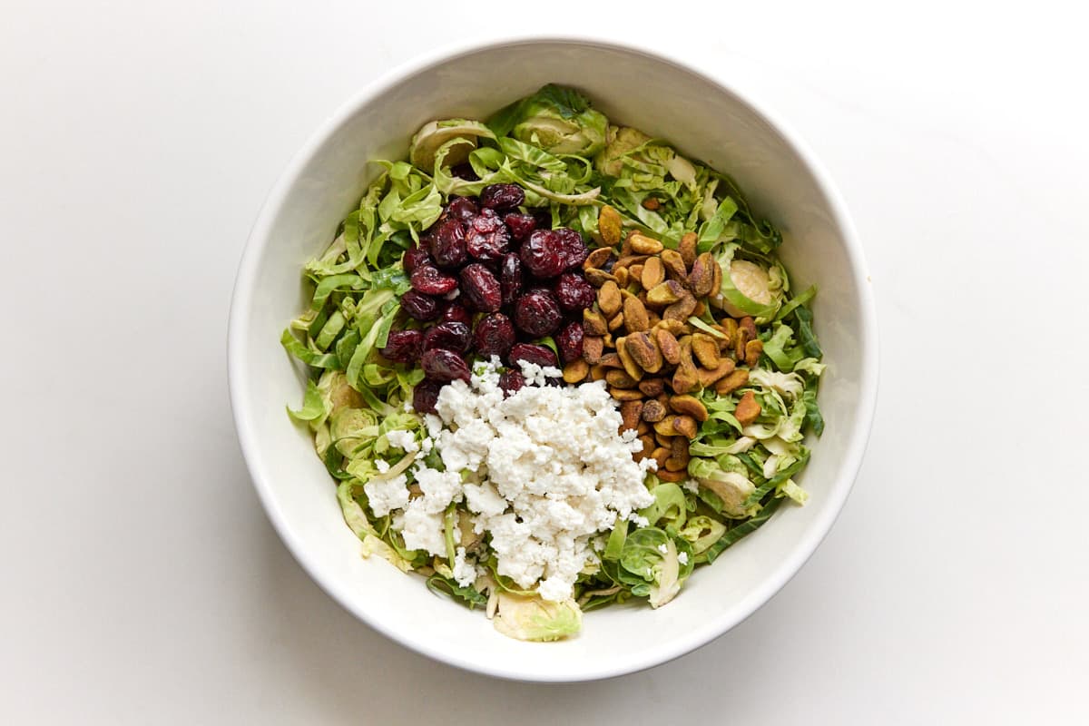 White bowl with shredded brussels sprouts, pistachios, craisins and feta cheese. 