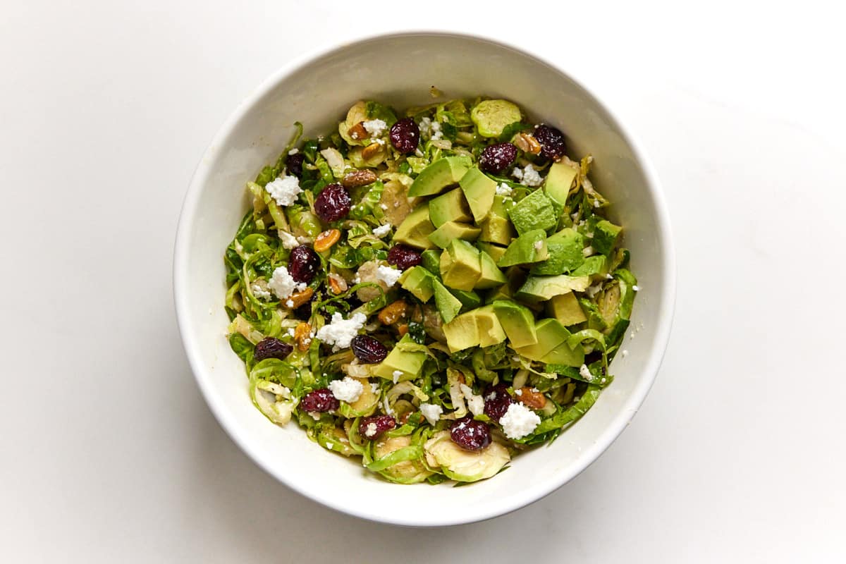 Shredded brussels sprouts salad with avocado in white bowl. 