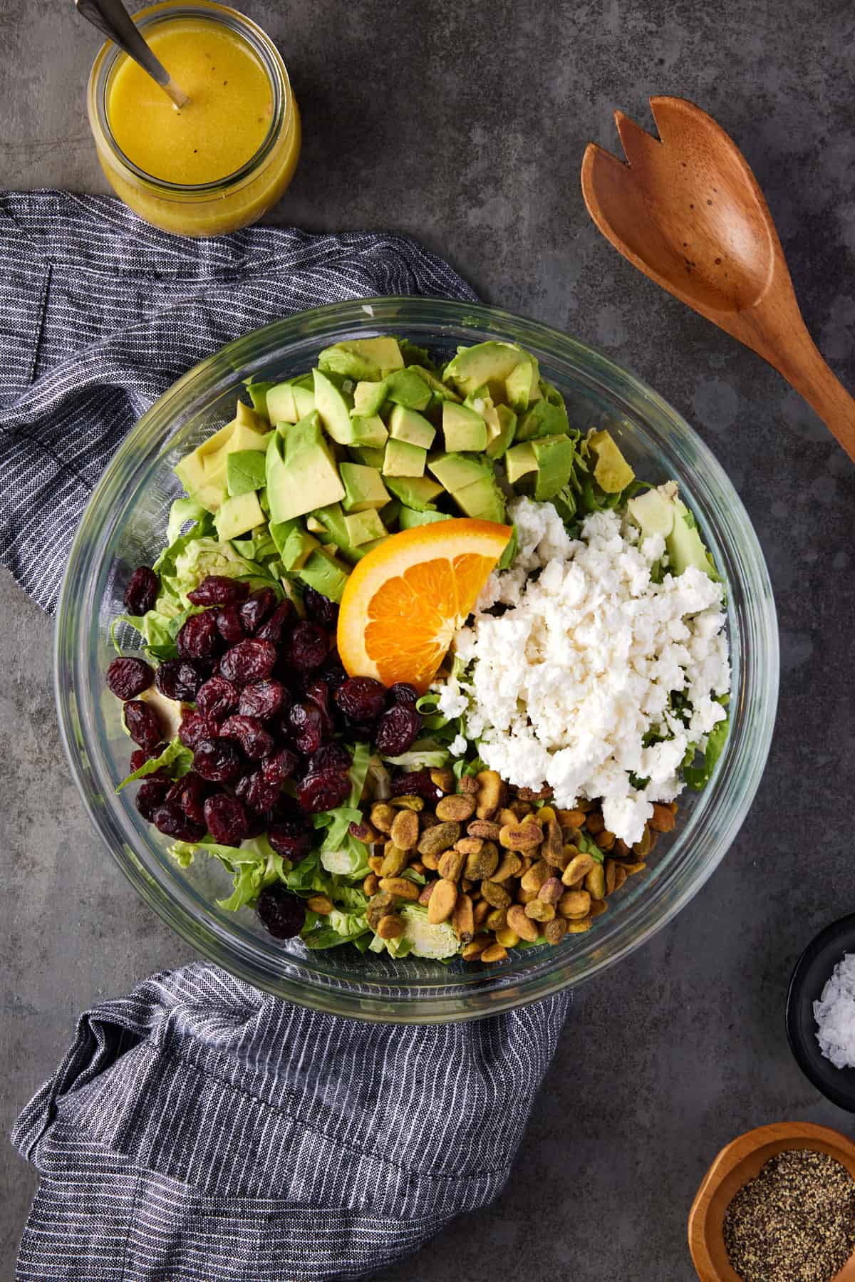 Shaved brussels sprouts salad with craisins, feta cheese, avocado and pistachios in glass bowl. 