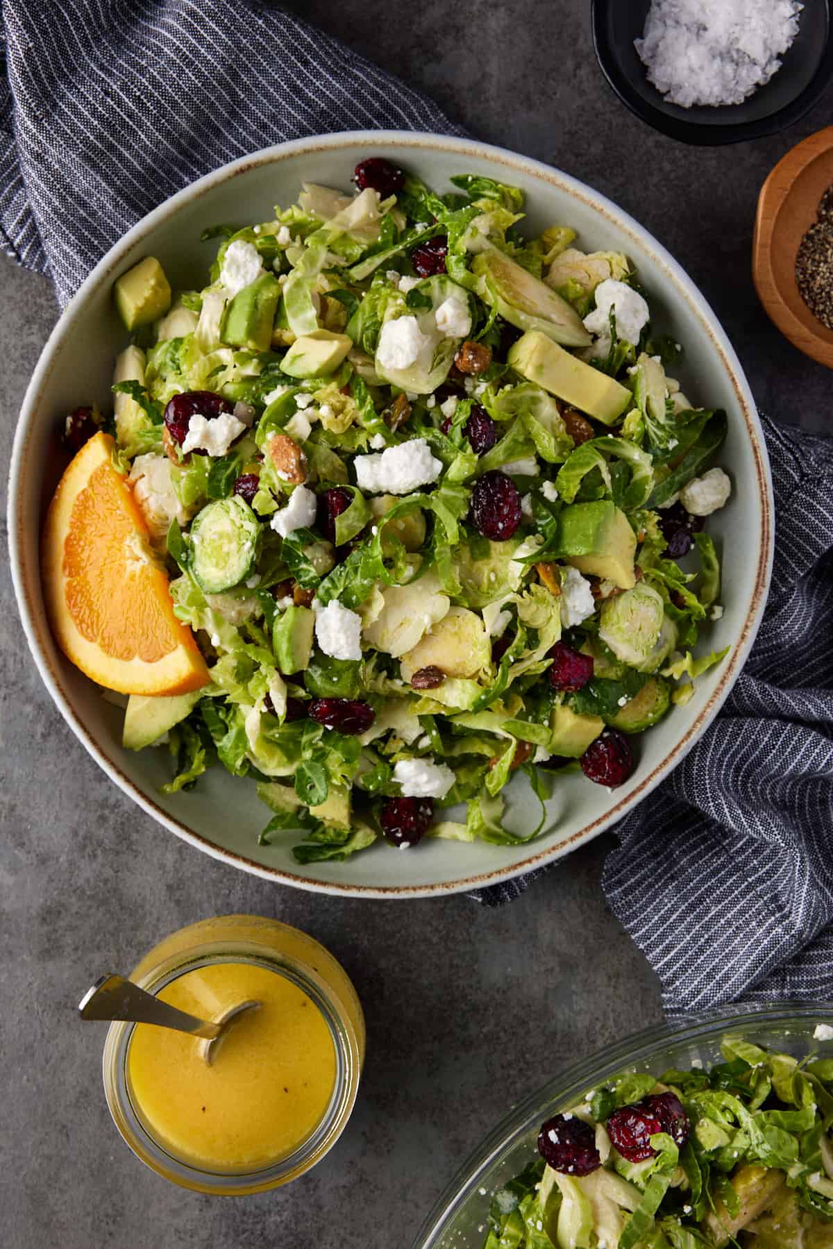 Large gray bowl filled with shaved brussels sprouts salad with a small glass jar of citrus vinaigrette. 