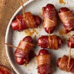 Bacon wrapped smokies with toothpicks on a cream plate.