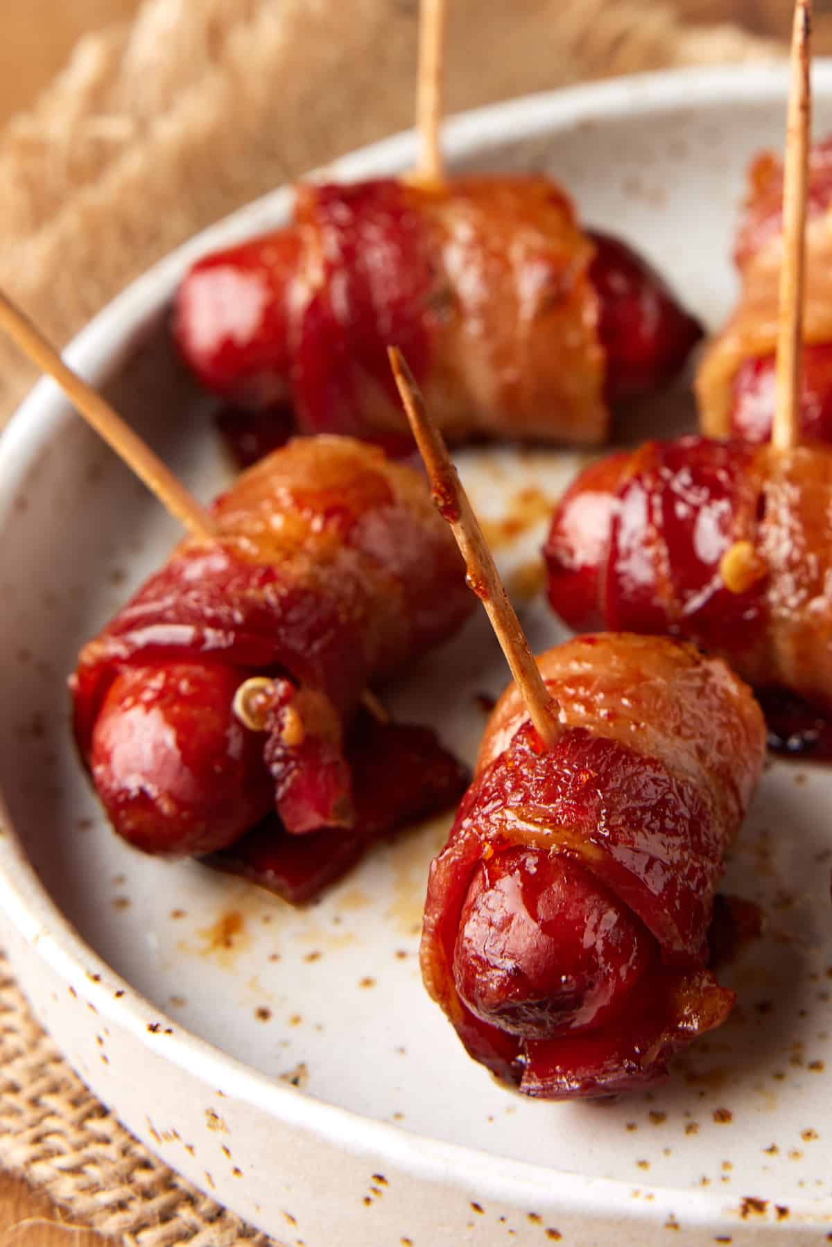 Bacon wrapped smokies skewered with toothpicks on a cream plate. 