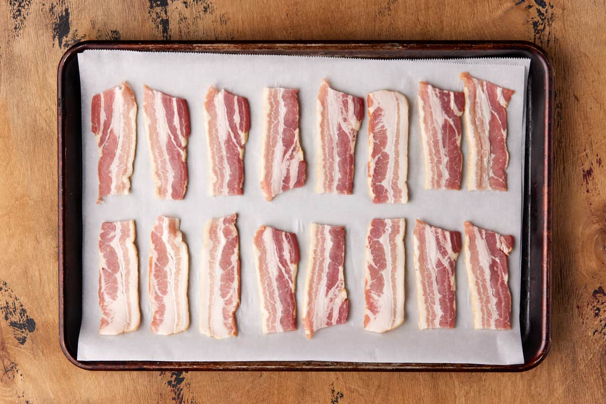 Raw bacon slices on a sheet pan lined with parchment paper. 